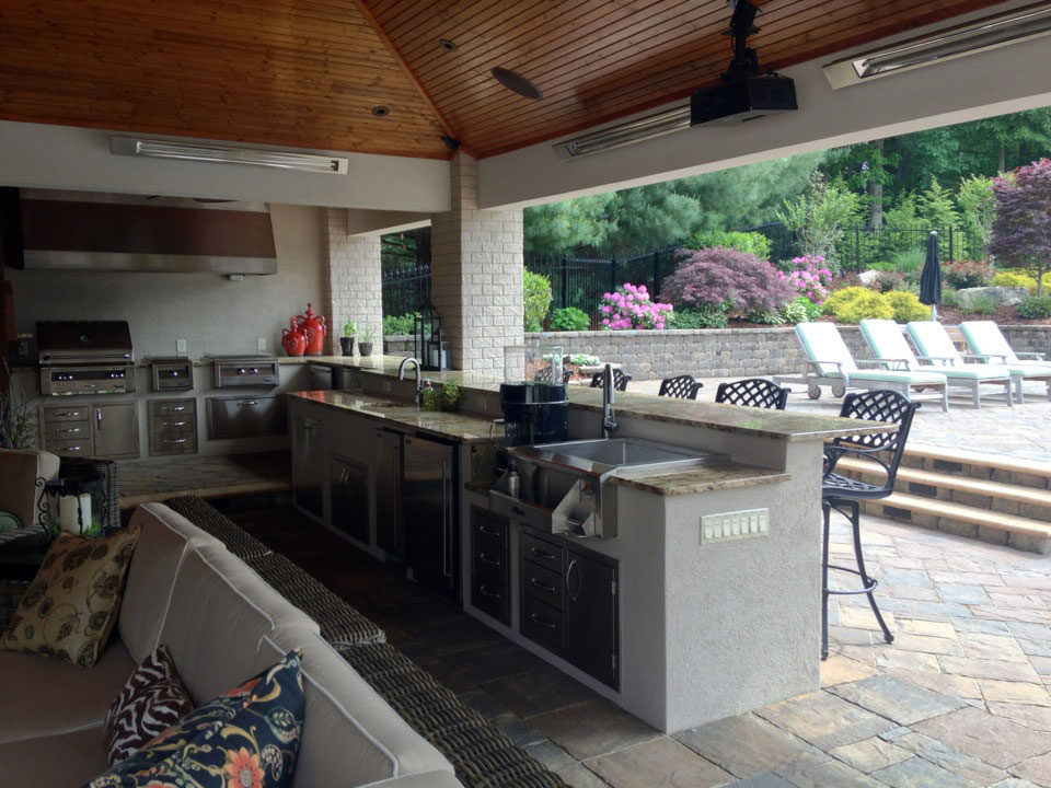 Outdoor bar with lighting and stone patio with professionally pruned yard